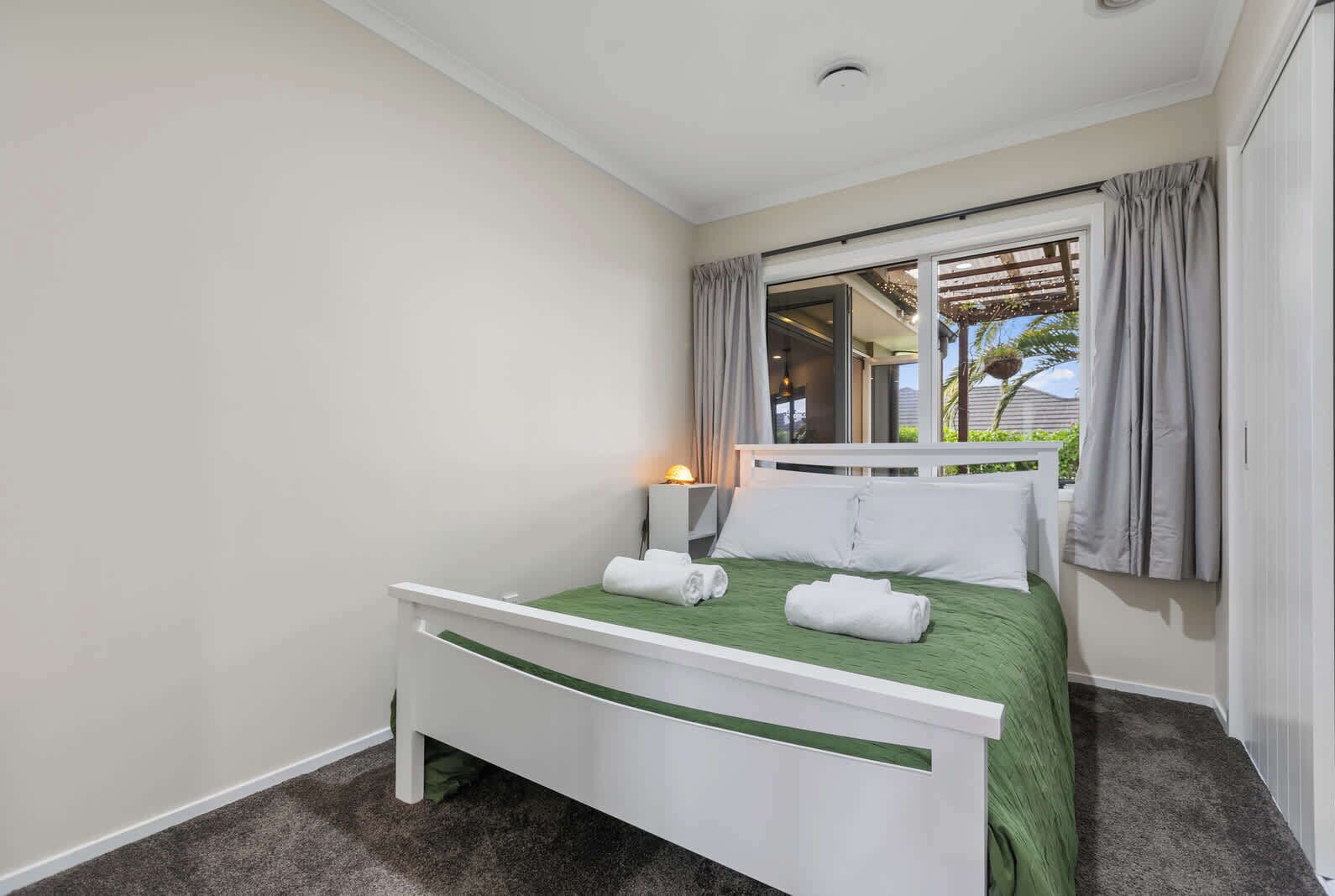 A hotel room with a bed, a nightstand, a window with curtains, and a view of the outside.