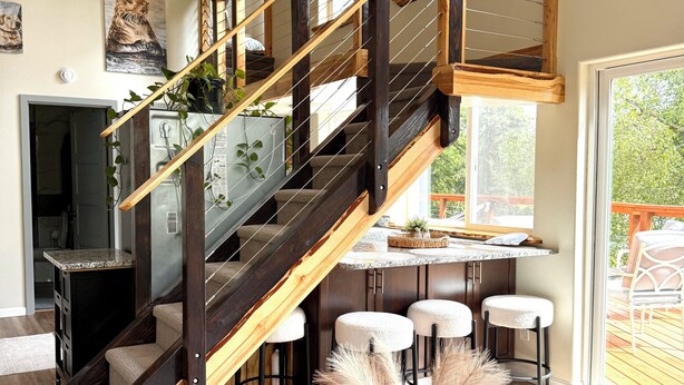Un interior moderno con una escalera de madera, una zona de cocina y un comedor con taburetes de bar.
