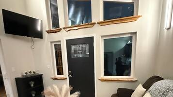 A living room with a dark brown sofa, a coffee table, a black TV mounted on the wall, and a black door with a window above it.