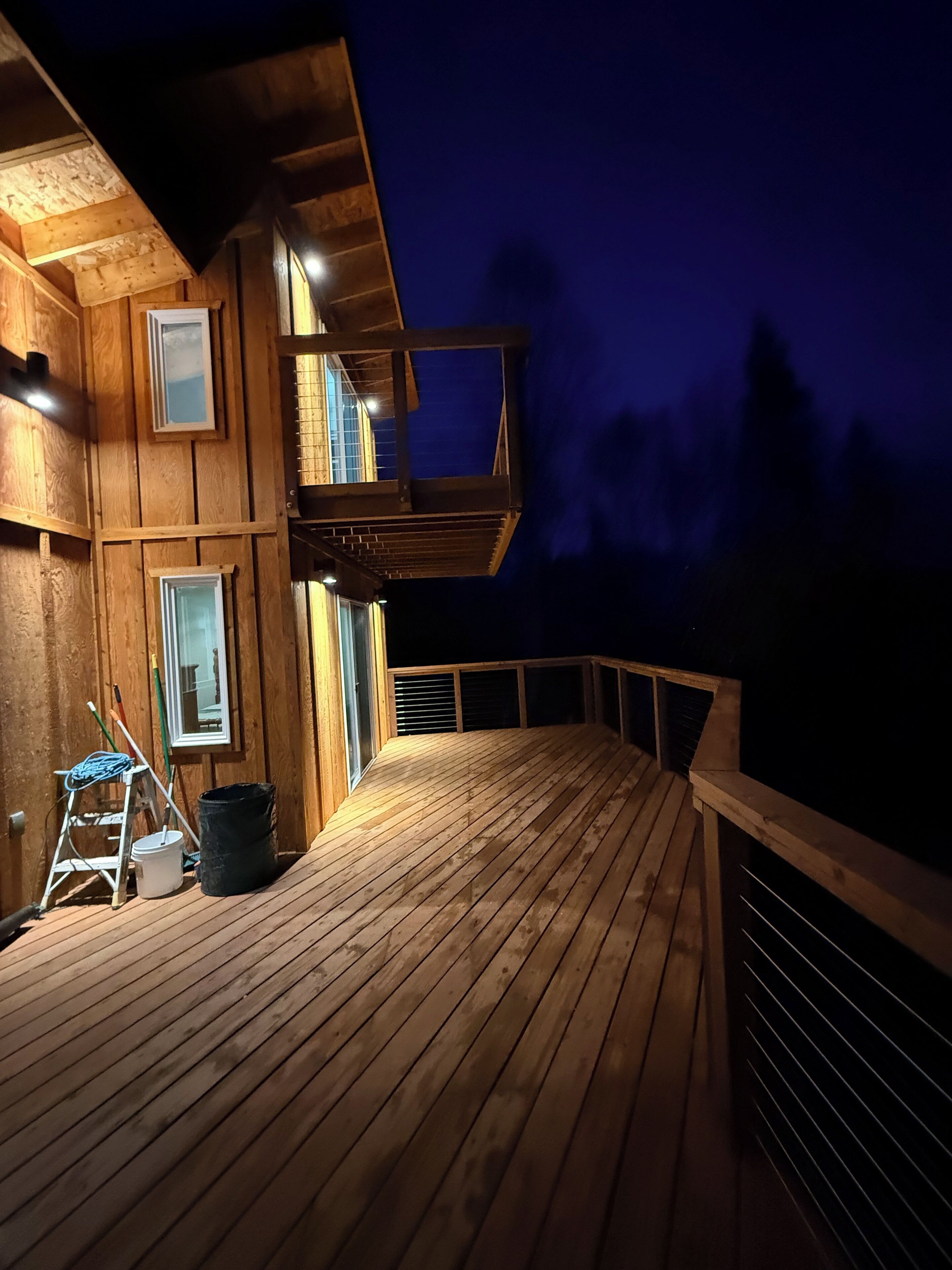 A wooden deck with railings, a ladder, and a bucket, likely for maintenance.