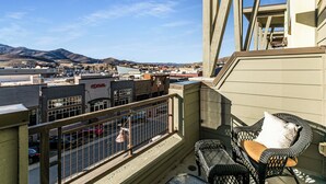 Ein Balkon mit Korbmöbeln, Blick auf eine Stadtlandschaft und Berge im Hintergrund.