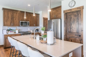 A kitchen with wooden cabinets, stainless steel appliances, a large island with stools, and pendant lighting. - Summer by the Lake! Beautiful Swimming Pool, Patio w Hot Tub and BBQ Nature Trails Hiking Biking (Hideout)