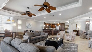 A spacious living room with a gray sofa, a coffee table, and patterned armchairs. There are ceiling fans, recessed lighting, and a kitchen in the background. - Stylish Gulf-Front Condo w/ Balcony & Pools (Miramar Beach)
