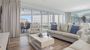 A modern living room with a sofa, coffee table, and a large window with curtains. - Exclusive beachfront: 2BR condo, pool, hot tub (Miramar Beach)
