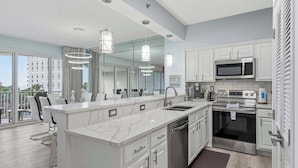 A modern kitchen with a large island, stainless steel appliances, and a view to the outside. - Exclusive beachfront: 2BR condo, pool, hot tub (Miramar Beach)
