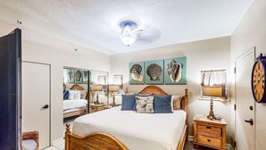 A bedroom with a wooden bed, a nightstand, a mirror, and wall art. - Beachfront Luxury (Miramar Beach)