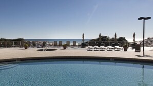 A pool area with lounge chairs and umbrellas, a clear view of the ocean, and a tiled deck. - Beachfront Luxury (Miramar Beach)