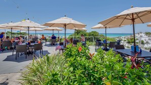 An outdoor patio with tables and chairs, surrounded by umbrellas, overlooking a beach. - Exclusive beachfront: Gulf views, sleeps 6 (Miramar Beach)