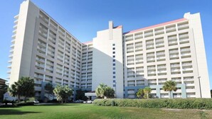 A multi-story hotel with a modern design, featuring a central courtyard with palm trees and a well-maintained lawn. - Beachfront condo with Gulf views & pool access (Miramar Beach)