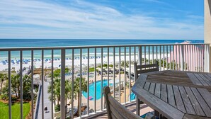 A balcony with a view of a beach, a pool, and a wooden table. - Beachfront condo with Gulf views & pool access (Miramar Beach)