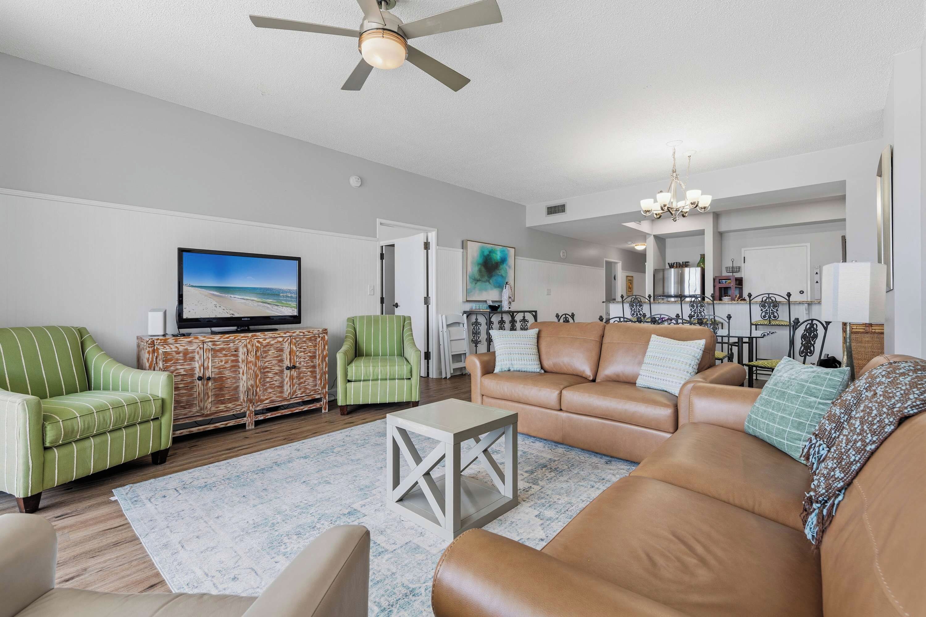 A living room with a television, green striped armchairs, a brown leather sofa, and a ceiling fan.