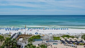 A beach resort with sun loungers, umbrellas, a pool, and a wooden boardwalk. - Beachfront condo with Gulf views & pool access (Miramar Beach)