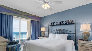 A bedroom with a bed, two nightstands, a chair, a ceiling fan, and a view of the sea. - Beachfront condo with Gulf views & pool access (Miramar Beach)