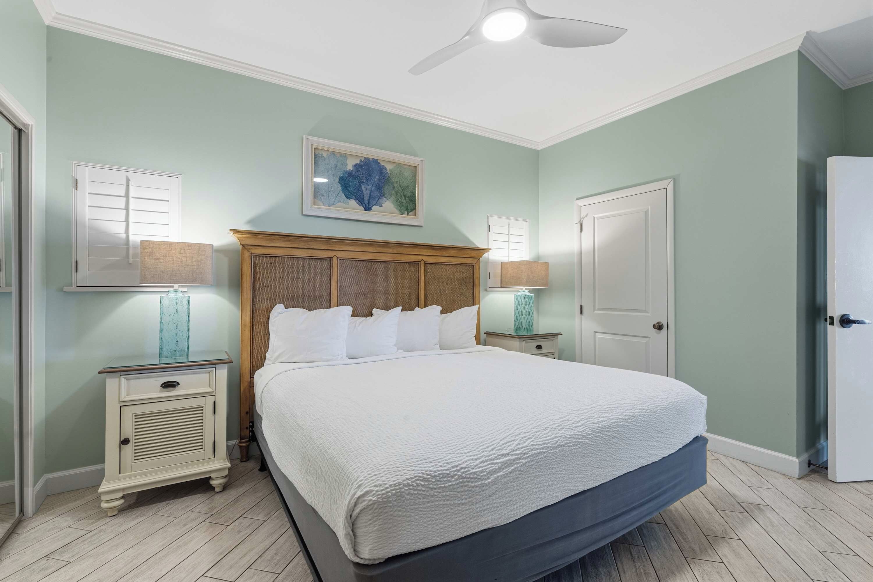 A bedroom with a large bed, two bedside tables with lamps, a ceiling fan, and a door.
