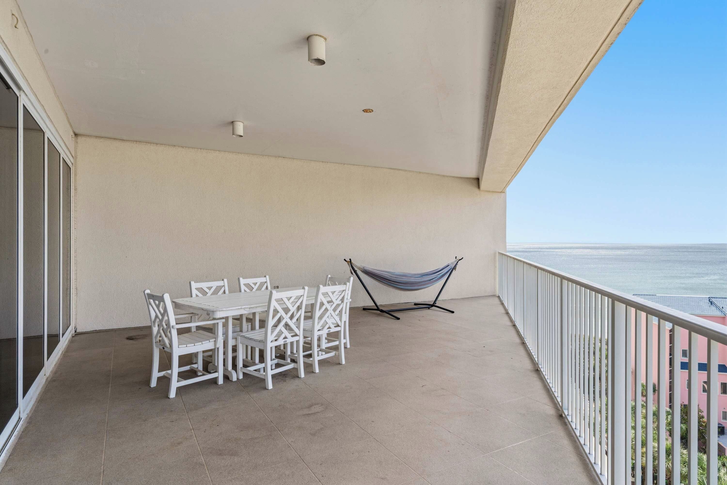 A balcony with a table and chairs, a hammock, and a view of the ocean.