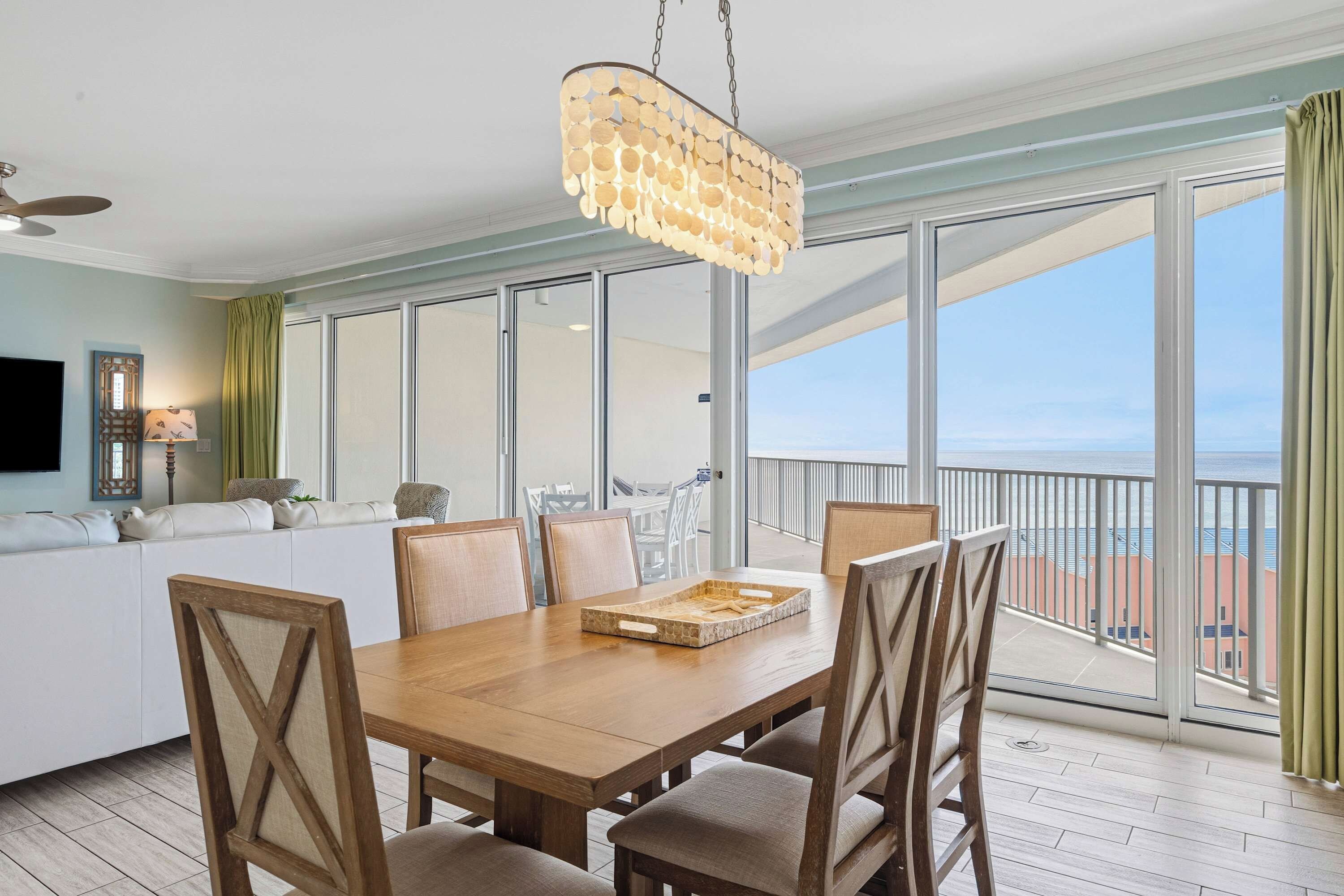 A spacious dining area with a wooden table and chairs, a hanging light fixture, and a view of the ocean through large windows.