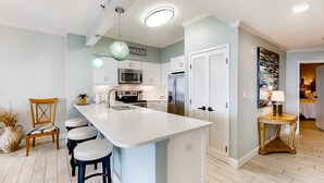 A modern kitchen with a central island, bar stools, a microwave, refrigerator, and a hanging light fixture. - Beachfront escape with Gulf views, pool access (Miramar Beach)