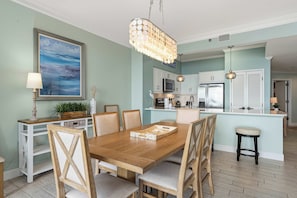 A dining area with a wooden table and chairs, a chandelier, and a kitchen in the background. - Beachfront escape with Gulf views, pool access (Miramar Beach)