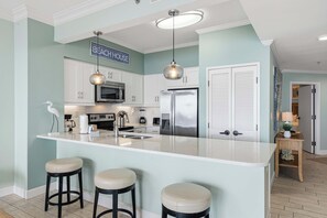 A kitchen with a central island, white cabinets, stainless steel appliances, and pendant lighting. - Beachfront escape with Gulf views, pool access (Miramar Beach)