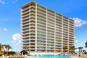 Un hotel moderno de altura con varios balcones, piscina y palmeras.