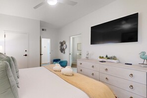Un dormitorio con una cama, un aparador, un televisor de pantalla plana y una puerta que da a otra habitación.