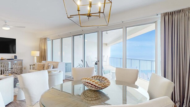 Ein modernes Hotelzimmer mit einem Glastisch, weißen Stühlen, einer dekorativen Schale, einem Flachbildfernseher und einem Balkon mit Blick.