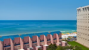 Ein Küstenhotel mit mehreren rosa Gebäuden, einem Strand mit Sonnenschirmen und freiem Blick auf den Ozean.