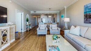 A spacious living room with a ceiling fan, a large flat-screen TV, a coffee table with magazines, and a sofa. - Oceanfront condo with breathtaking views (Miramar Beach)