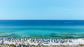 A beach with numerous umbrellas and sun loungers, a clear blue sea, and a few boats in the distance. - Oceanfront condo with breathtaking views (Miramar Beach)
