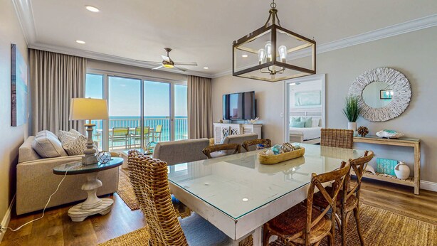 A spacious living area with a glass-top dining table, wicker chairs, a sofa, and a TV. - Oceanfront condo with breathtaking views (Miramar Beach)