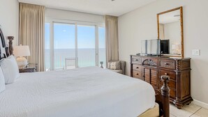 Ein Hotelzimmer mit einem großen Bett, einem Deckenventilator, einer Holzkommode, einem Fernseher und einem Balkon mit Meerblick.