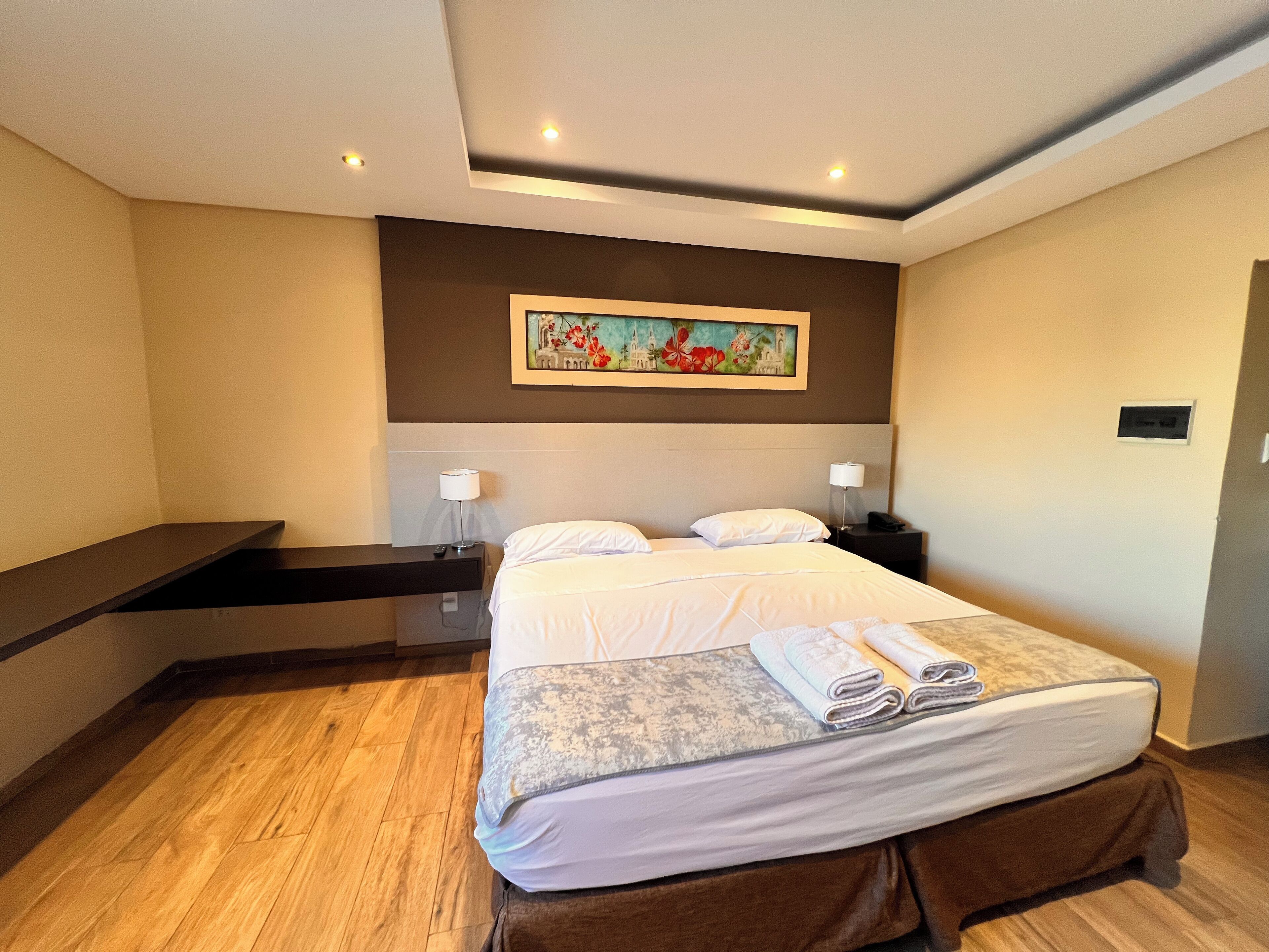 Una habitación de hotel con una cama, mesitas de noche, un cuadro en la pared y suelo de madera.