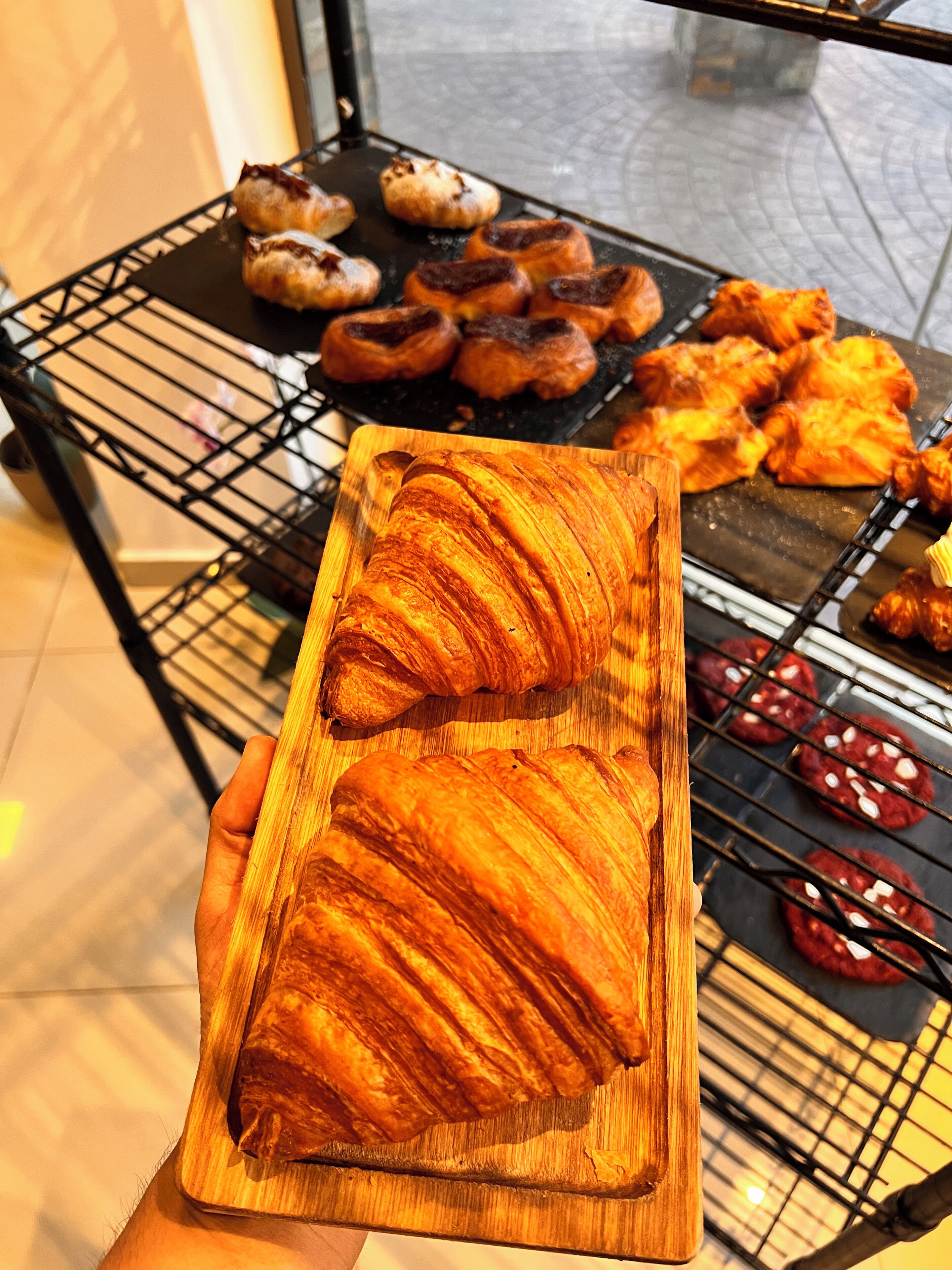 A wooden board with croissants and a rack of baked goods.