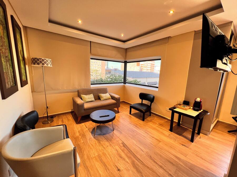 A modern living room with a sofa, two armchairs, a coffee table, and a TV mounted on the wall.