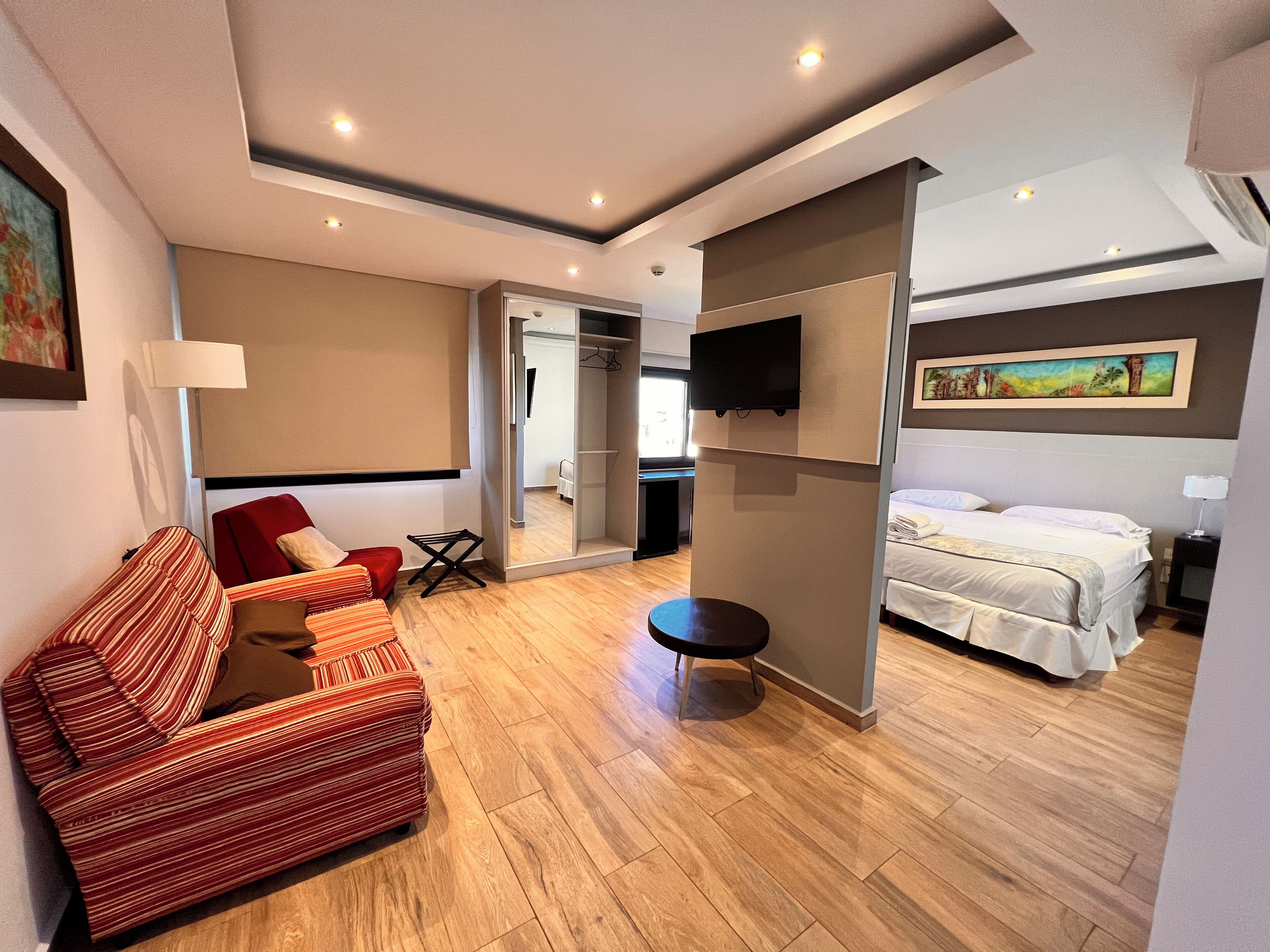 A hotel room with a sofa, a bed, a TV, and a mirror.