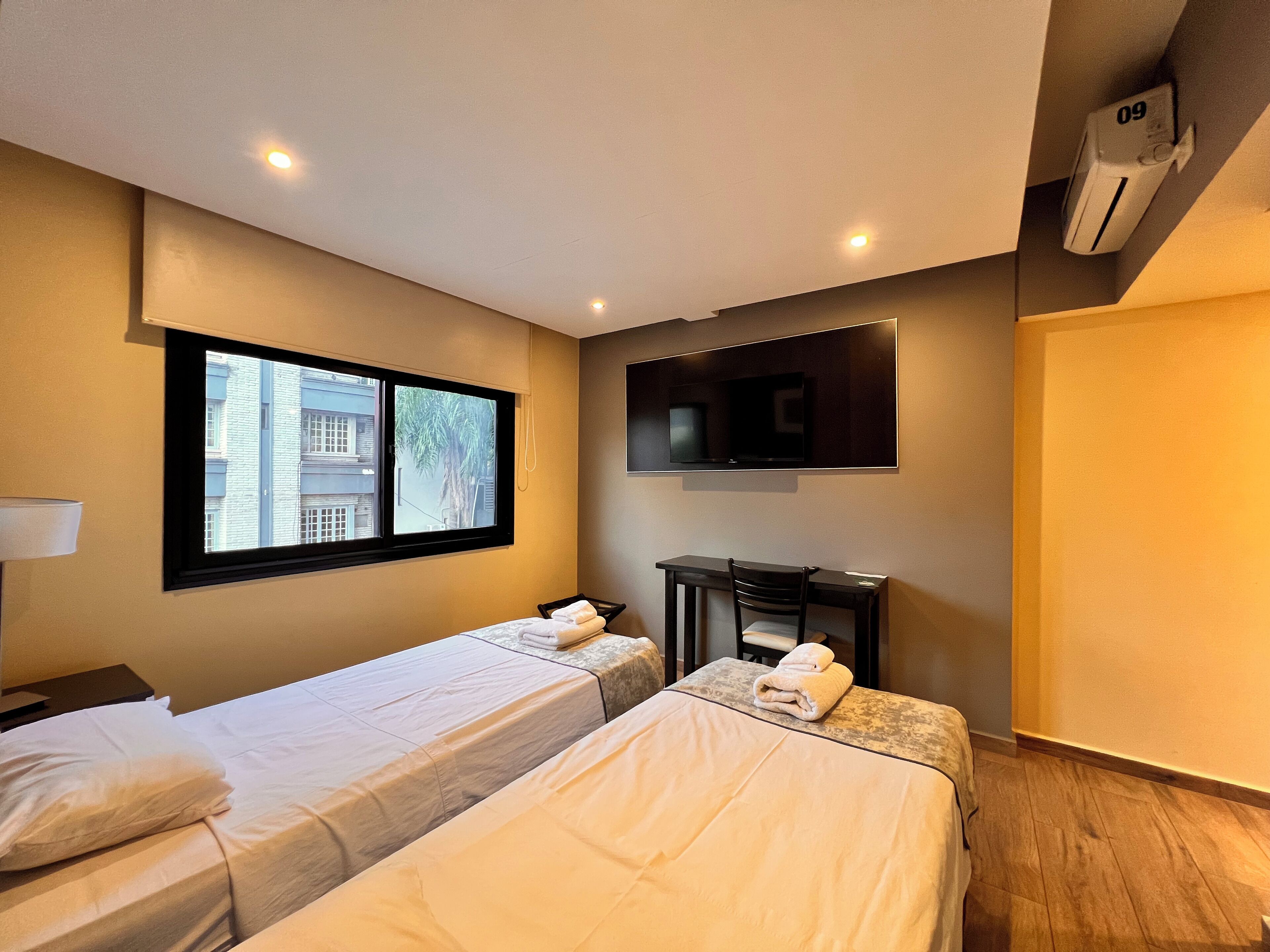 A hotel room with two beds, a desk, a TV, and a window.