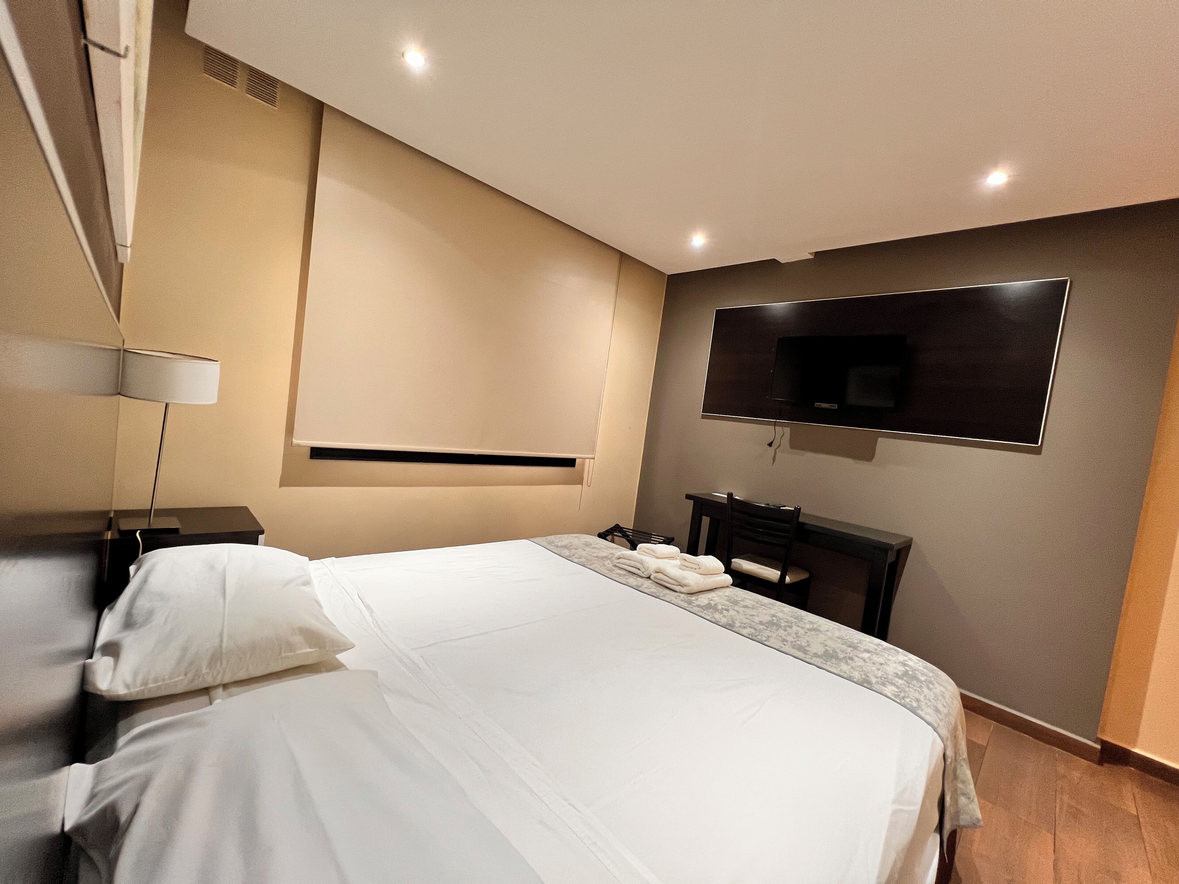 Une chambre d’hôtel moderne dotée d’un grand lit, d’un téléviseur à écran plat fixé au mur, d’un bureau avec une chaise et d’une lampe sur la table de chevet.
