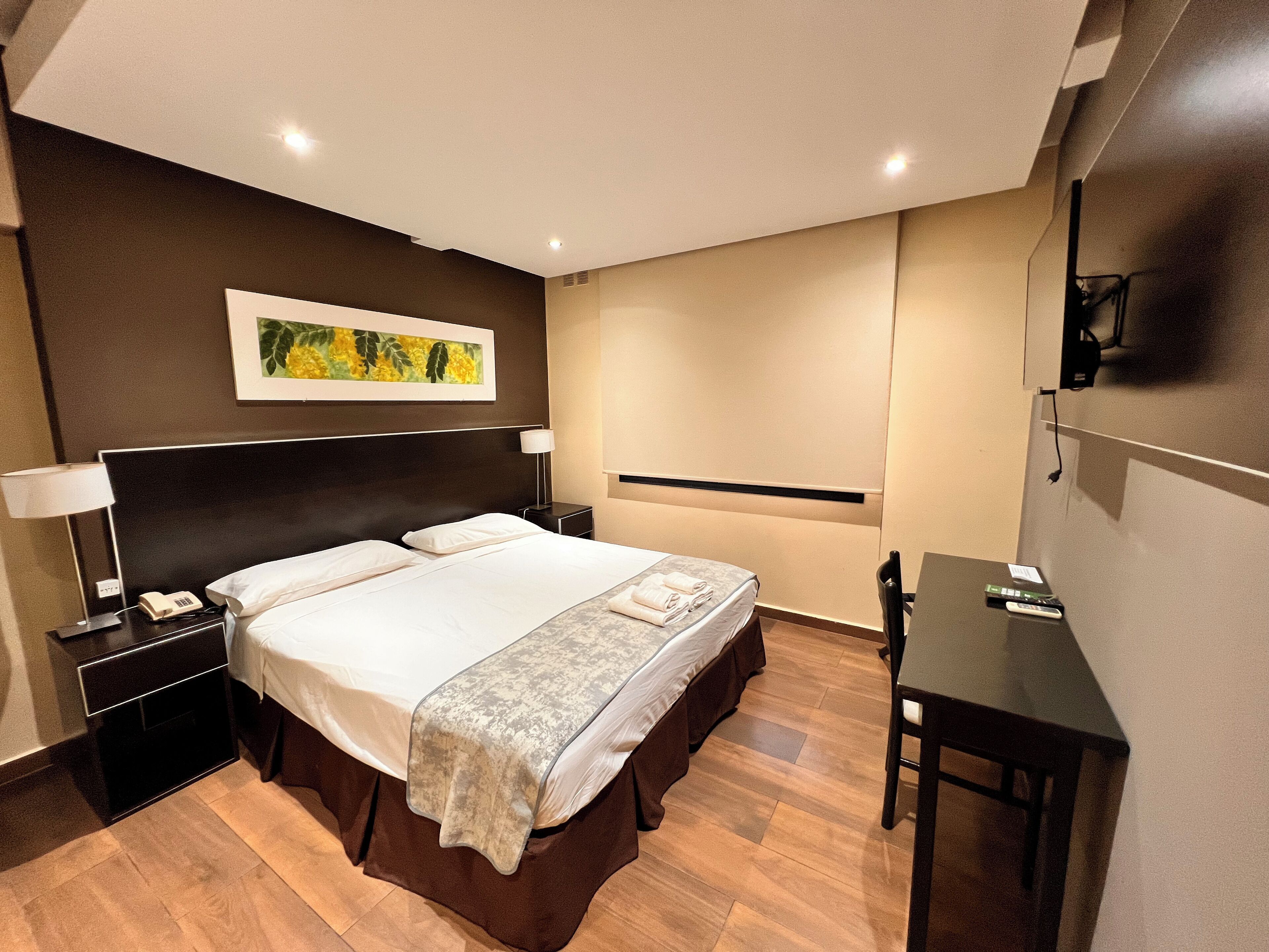 A hotel room with a large bed, bedside tables, a desk, and a TV.