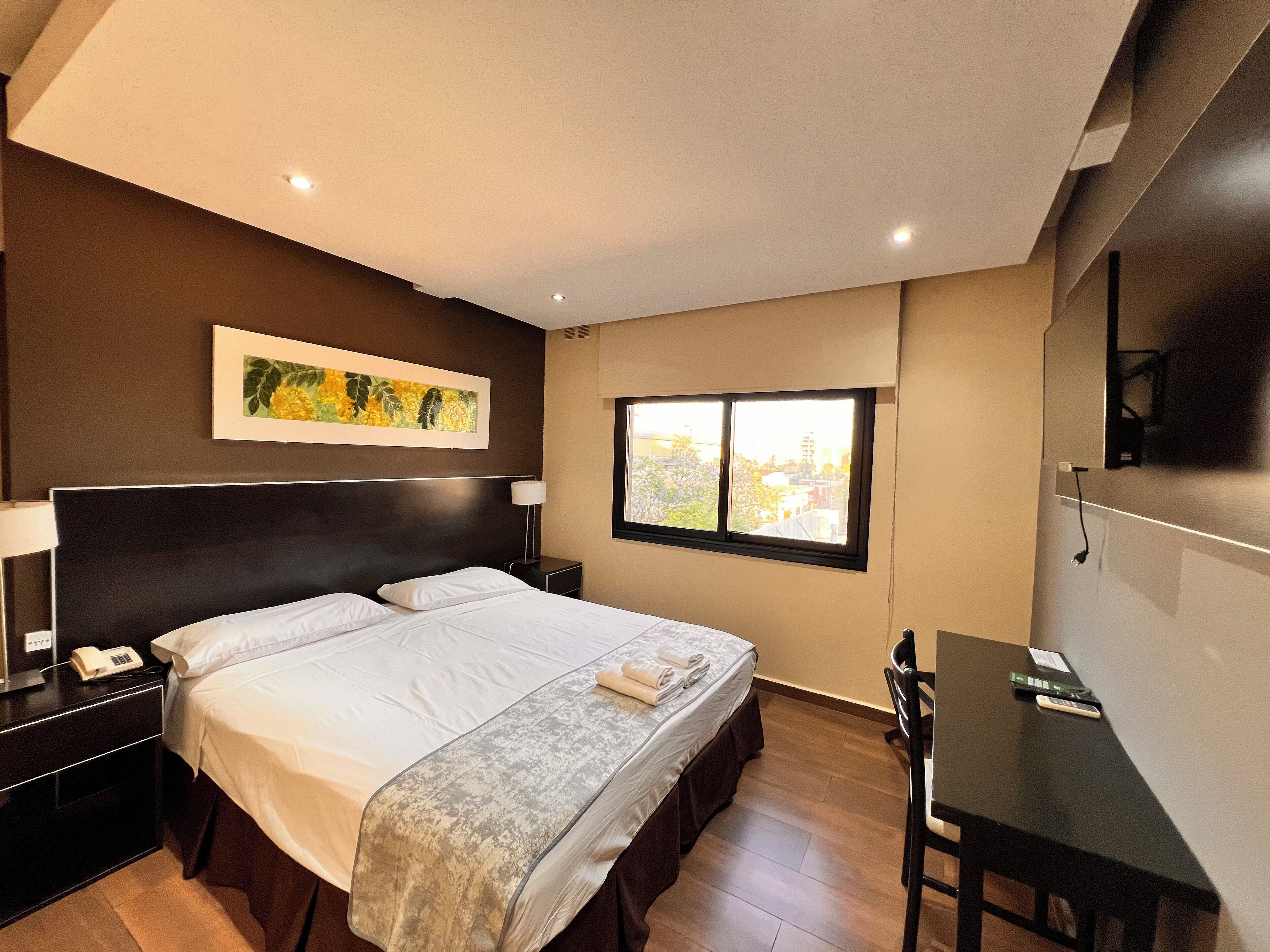 Una habitación de hotel con una cama grande, mesitas de noche, un escritorio y una ventana con vistas a la ciudad.