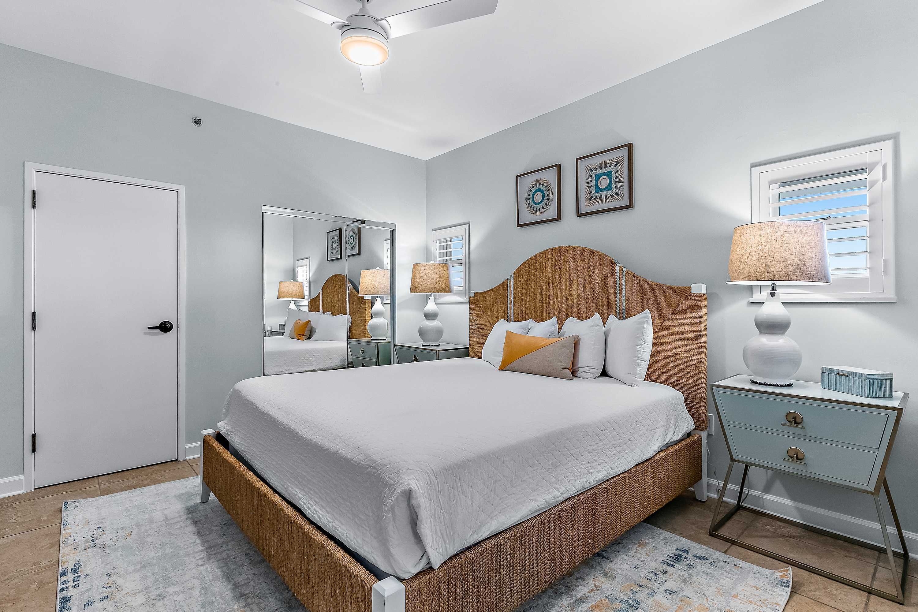 A bedroom with a large bed, a nightstand, a mirror, and a window with blinds.