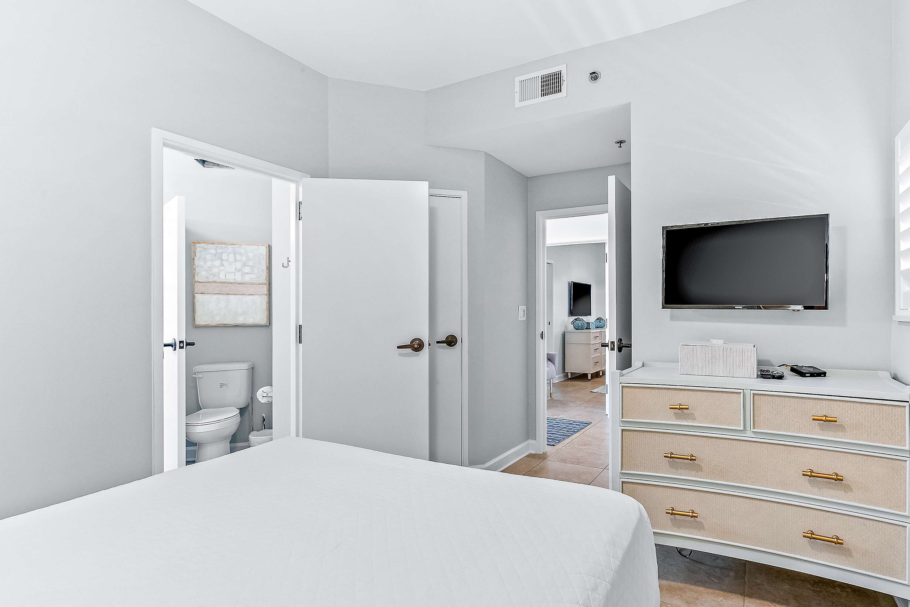 A modern bedroom with a bed, a TV mounted on the wall, and a dresser with drawers.