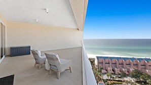 Een balkon met twee rieten stoelen en een kleine tafel, met uitzicht op een strand en een rij roze gebouwen.
