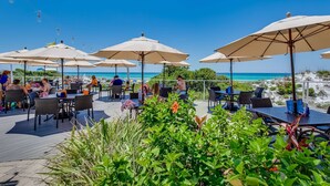 An outdoor seating area with tables and chairs, umbrellas, and a view of the ocean. - Gulf-front condo: 2BR, pools, direct beach (Miramar Beach)