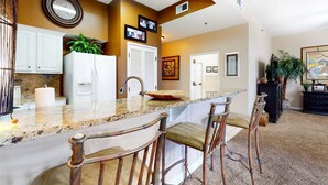 A kitchen with a granite countertop, white cabinets, a refrigerator, and a sink. There are three bar stools with cushioned seats. - Gulf-front condo: 2BR, pools, direct beach (Miramar Beach)