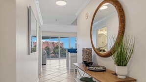 Un pasillo con un espejo grande, una consola de madera con una planta y vistas a un balcón con mobiliario exterior.