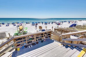 En strandutsikt med ett trädäck, strandstolar, parasoller och ett skohörn.