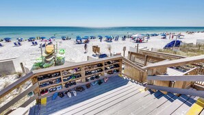 A beach view with a wooden deck, beach chairs, umbrellas, and a shoe rack. - Exclusive 2BR Beachfront | Gulf Views Balcony (Miramar Beach)