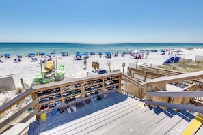 Blick auf einen Strand mit einer Holzterrasse, Liegestühlen, Sonnenschirmen und einem Schuhregal.