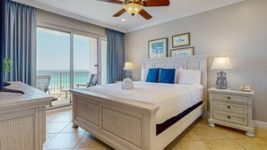 A bedroom with a large bed, a nightstand, a ceiling fan, and a view of the outdoors. - Exclusive 2BR Beachfront | Gulf Views Balcony (Miramar Beach)
