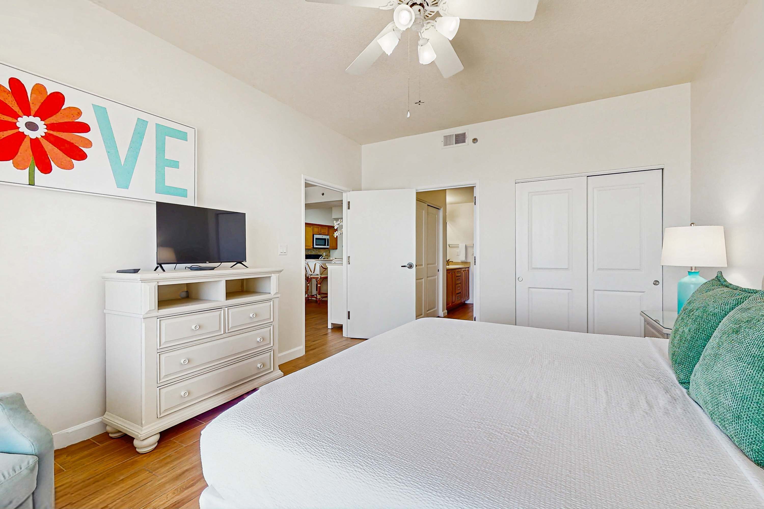 Ein Schlafzimmer mit Bett, Kommode, Fernseher und einem 'LOVE'-Schild an der Wand.
